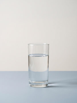Clear Glass Tumbler Partially Filled with Fresh Drinking Water on a Minimalist Light Neutral Surface, Simple Hydration and Healthy Lifestyle Concept Photography