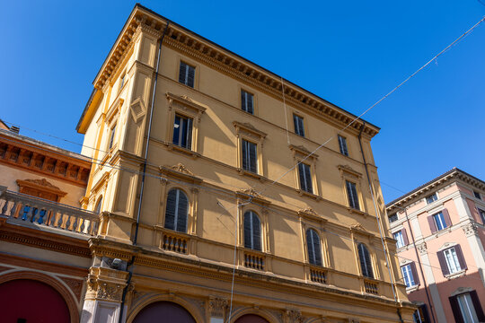 Ornate yellow neoclassical building facade with arched shutters against blue sky in Bologna, Italy