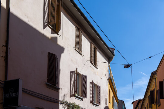 Bologna, Italy - October 14, 2026: Old building facade with brown wooden shutters and restaurant sign under blue sky in Bologna, Italy