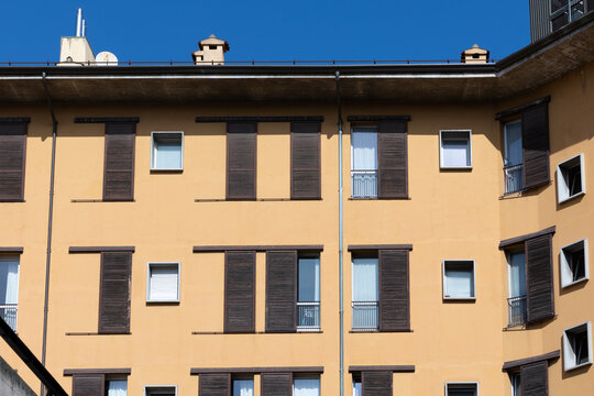 Ochre residential building facade with brown wooden shutters against a deep blue sky in Bologna, Italy