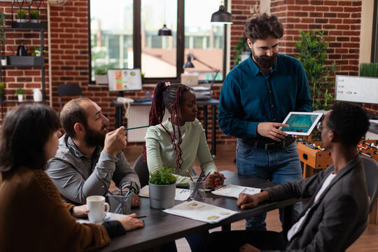 Tablet, presentation and teamwork in a brick-wall office as a standing man points to digital charts and a seated colleague responds. Business communication, data review and collaborative planning.