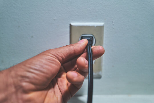 Hand Pulling a Black Power Cord from a Wall Outlet