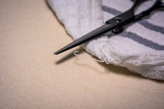 Black scissors lie close to a loose thread on a reusable towel. DIY home textile repair, everyday household chores, housekeeping lifehacks and zero waste lifestyle.