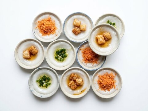 Traditional Vietnamese banh beo steamed rice cakes in small ceramic dishes topped with shrimp flakes and crispy pork cracklings on a white background
