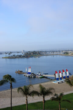 Bird-eye view of Sail Bay in Mission Bay, San Diego, featuring a sandy beach, palm trees, and sailboats docked at a pier