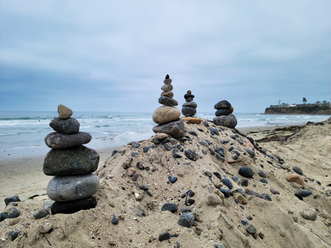 Balanced beach pebble pyramids or cairns standing as calm symbols of spiritual harmony and wellness built on top of a small rock and sand mound in Tourmaline surfing park, San Diego, California