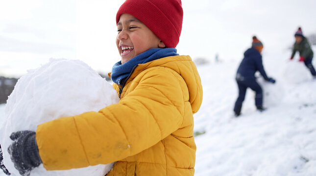 Pacific Islander child hugging a giant snowball in yellow coat and red hat, laughing on a snowy hillside for joyful holiday posters.