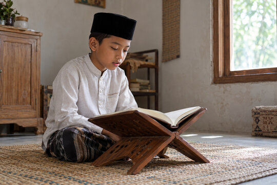 Young Indonesian boy reciting holy book on wooden stand in Ramadan
