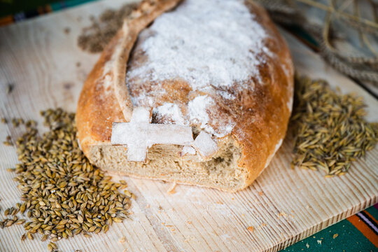Close up of traditional harvest bread loaf with a salt cross decoration and scattered cereal grains on a wooden table.