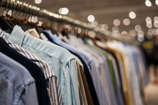 Row of men's shirts hanging on clothing racks in a retail store with a soft bokeh background