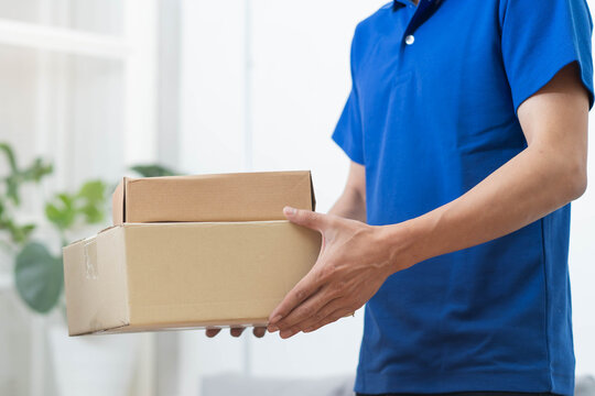 Delivery man in blue uniform holding cardboard boxes close up, professional courier carrying parcel post packages for customer service
