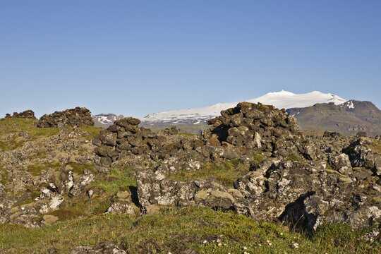 "Fiskibyrgi" stone huts thought to be used as shelter by fishermen over 700 years ago, Mt. Snaefellsnessjoekull in the background, Snaefellsness Peninsula, Iceland, Atlantic Ocean