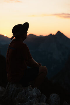 Young man sitting on a rocky peak at sunset, enjoying the breathtaking mountain view. Concept of freedom, adventure, and achievement in the wilderness.