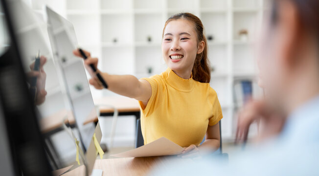 Smiling Asian Businesswoman Pointing Pen at Computer Screen in Office Meeting
