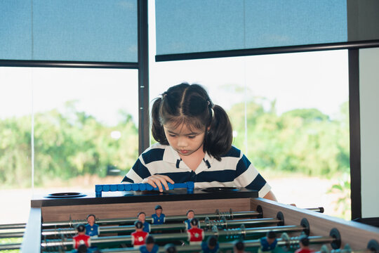 Young girl with pigtails concentrating on playing table game with focus in bright modern room with large windows
