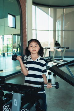 Young girl with ponytails exercising with dumbbell in modern gym wearing striped polo shirt focused on strength training