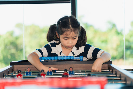 Young girl focused playing foosball alone at indoor game table in bright natural light near window background
