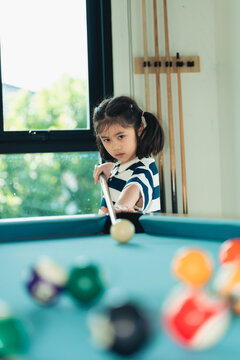 Young girl focused on aiming with a cue stick while playing billiard indoor during daytime