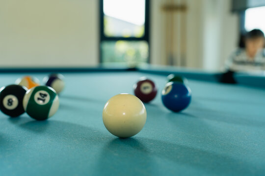 Close-up of white billiard ball on blue felt pool table with blurred colorful billiard balls and player in background
