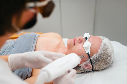 Aesthetic therapist performing laser facial treatment on client
