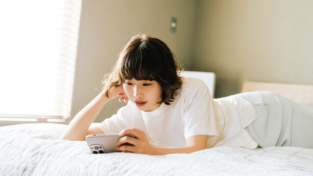 ベッドに寝転んでスマートフォンを使う女性