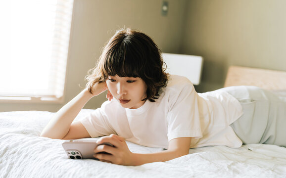 ベッドに寝転んでスマートフォンを使う女性