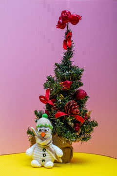 snowman crocheted from yarn, placed on a colorful background next to a Christmas tree