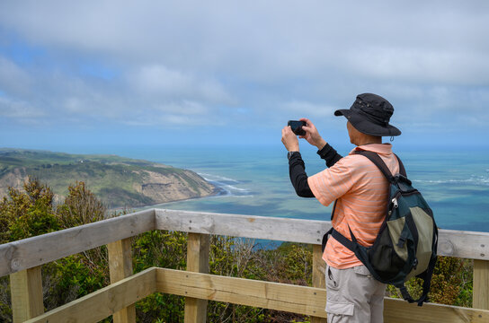 Hiker taking photos of Manuka Harbour and Manuka Heads from Mount Donald McLean summit. Waitakere Regional Park. Auckland.
