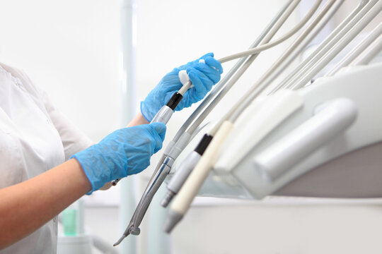 Disinfection of dental equipment. Dentist's hands in blue gloves hold dental handpiece next to equipment. Clinic instruments