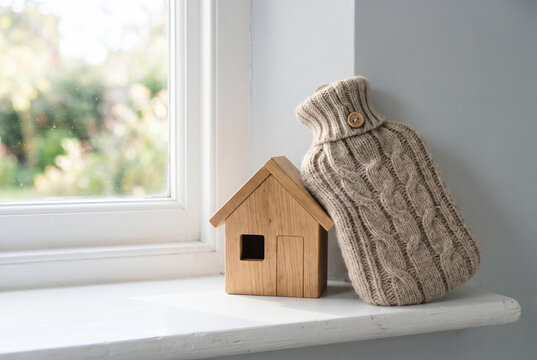 Knitted hot water bottle hugging a small wooden house on a windowsill