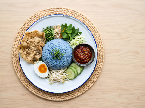 Blue rice with fresh herbs, salted egg and fish crackers on a plate