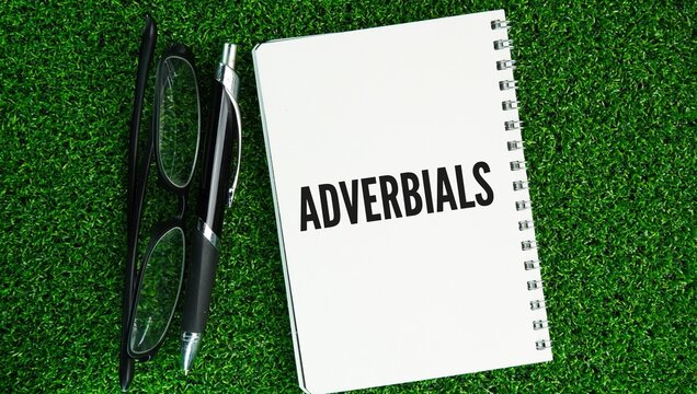 Glasses, pen and paper with adverbial words is any word, phrase, or clause that modifies or gives more information about a verb, adjective, adverb, or an entire sentence.