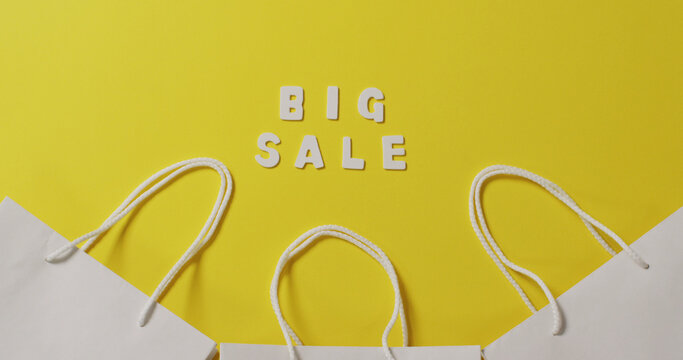 Big sale text in white and gift bags with string handles on yellow background