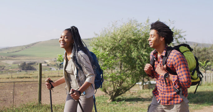 Happy african american couple with backpacks, hiking with trekking poles together, slow motion
