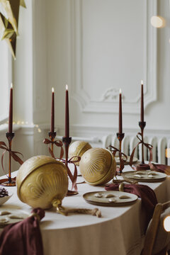 Elegant Christmas table setting with golden baubles, burgundy candles, and festive decor in a bright dining room for winter holiday celebrations