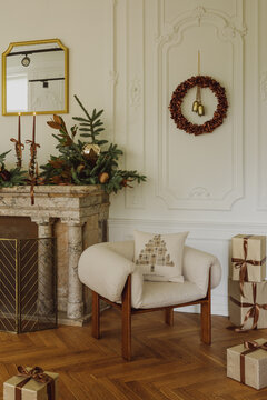 Elegant Christmas living room interior with a cozy armchair, wrapped gift boxes, decorated fireplace mantel, festive wreath, and warm holiday decor