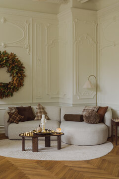 Elegant and cozy modern living room interior decorated for winter holidays with a comfortable white sofa, wooden coffee table, and festive wreath on the wall