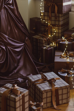 Elegant Christmas presents stacked under a brown draped tree with warm fairy lights creating a cozy festive atmosphere for holiday celebration and gifting