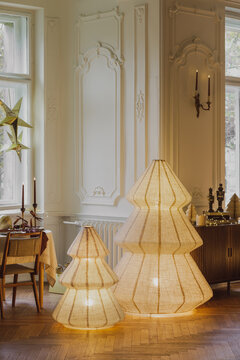 Elegant scandinavian holiday interior with glowing paper tree lamps, festive table setting, classic molding, and cozy winter atmosphere