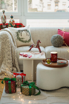 A warmly lit living room decorated for the Christmas holidays, featuring numerous wrapped gifts, a comfortable sofa with knit blankets, and festive decor for seasonal concepts