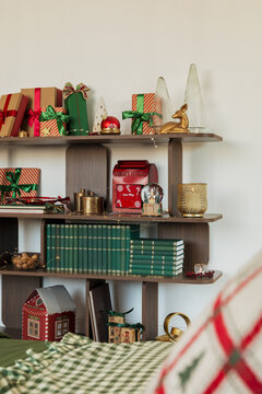 Cozy living room interior decorated for Christmas with wrapped presents, green books, decorative figurines and a festive mailbox on a wooden shelf unit