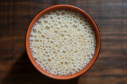 Flaxseed smoothie or protein shake with foam in ceramic cup, closeup. Healthy vegan beverage or protein milkshake with rich froth in clay cup, top view macro on dark wooden background