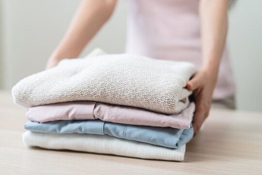 Close up of a woman holding a stack of clean folded clothes.