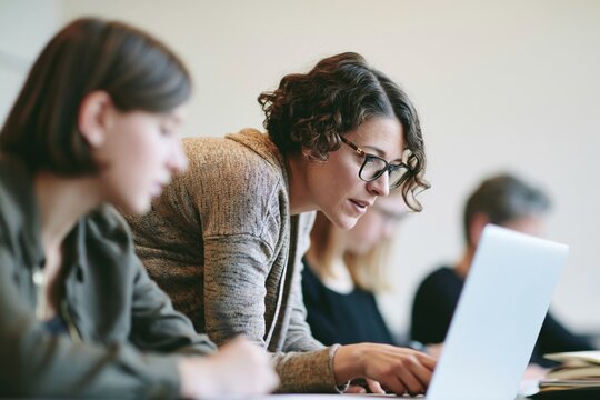 Mentor providing guidance to student at laptop, collaborative education in classroom setting