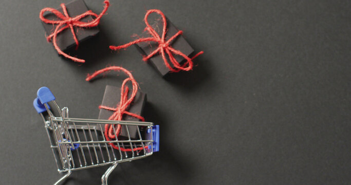 Three black gifts tied with red string and shopping cart on black background with copy space