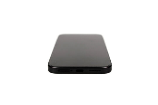Low angle close up of the bottom edge of a modern generic black smartphone resting on a white surface. Shows the USB-C charging port, speaker grille holes, and SIM tray. Minimalist matte black design 