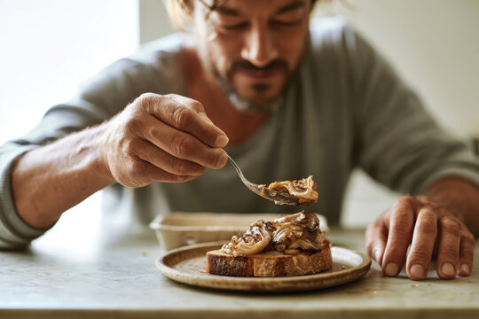 A man is applying a gourmet spread onto toasted bread, capturing a moment of culinary delight, showcasing the intimacy of food preparation and personal enjoyment.