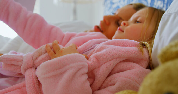 Side view of young Caucasian mother and daughter reading story book on bed in a comfortable home