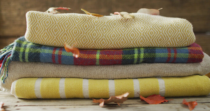 Image of folded blankets and autumn leaves on wooden background