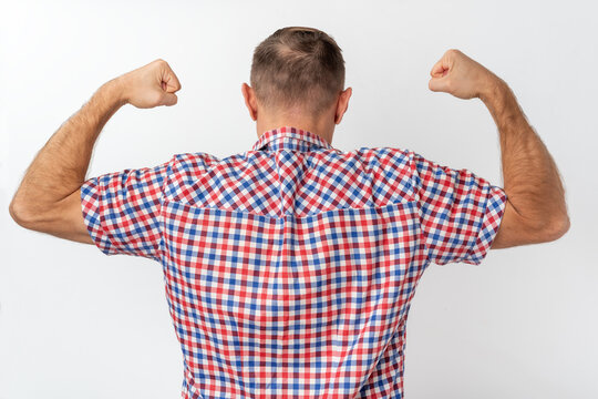 Man seen from behind, flexing biceps and expressing power, determination, and masculinity while wearing a red and blue plaid shirt against a white background